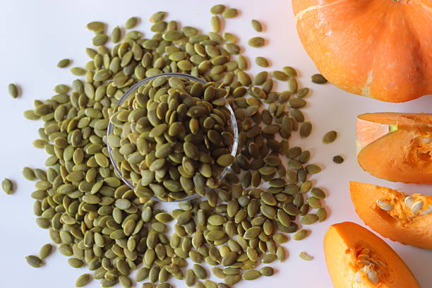 istock Glass jar filled with green pumpkin seeds or pepitas on a white surface, surrounded by scattered seeds 2227184604