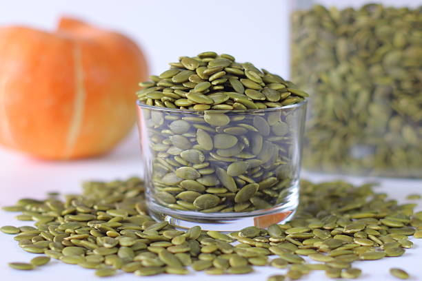 istock Glass jar filled with green pumpkin seeds or pepitas on a white surface, surrounded by scattered seeds 2227184636