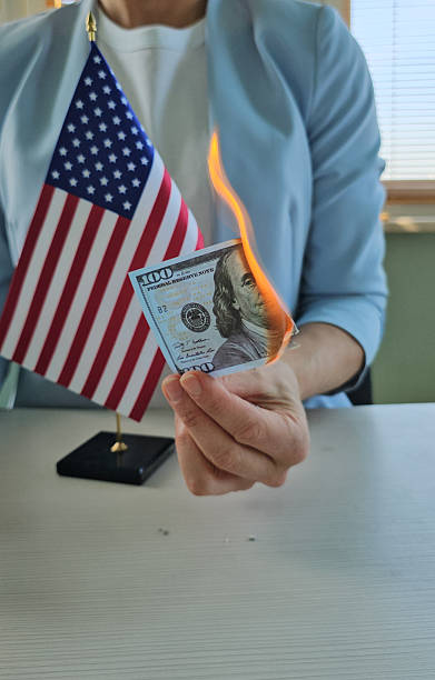 istock A person is holding a dollar bill that is on fire while standing beside a small American flag concept 2227194563