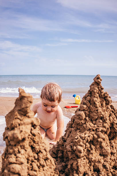 A young girl building a sandcastle on a seaside beach, creating shapes from wet sand under the bright summer sun.