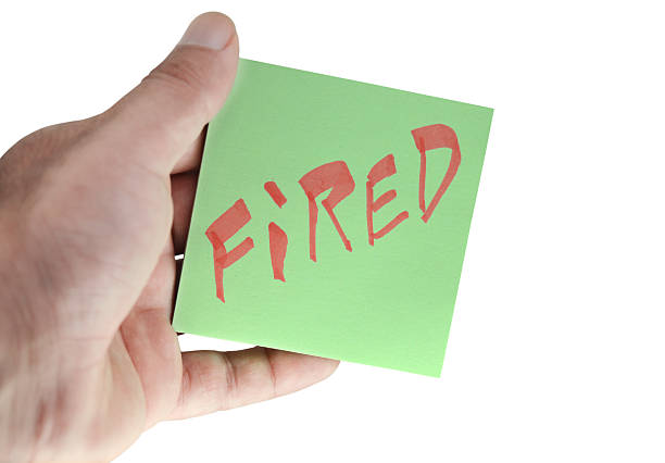 Cut out of one hand holding a green sticky note or adhesive slip with text FIRED, isolated over white background for firing, employee downsizing, office company headcount cuts, recession, unemployment, job loss posters, banners.