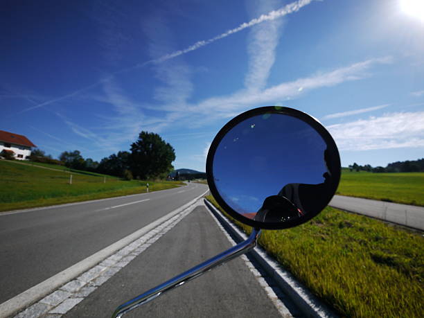 Mirror on a car is reflecting the sky and the road. The sky is blue and the road is empty