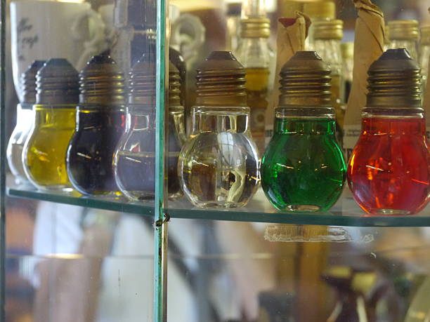Shelf of glass bottles with different colored liquids inside. The bottles are arranged in a row, with some bottles being taller than others. The bottles are of different shapes and sizes