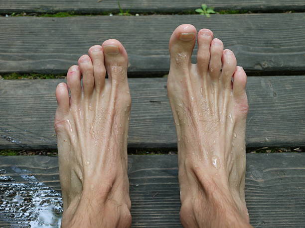 Man's feet with a lot of sweat on them. The feet are on a wooden surface, and the man is in a relaxed and comfortable position. Scene is casual and laid-back