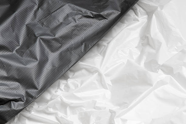 istock Crumpled black plastic film and white close up, texture of packaging material, plain polyethylene background with highlights 2227206441