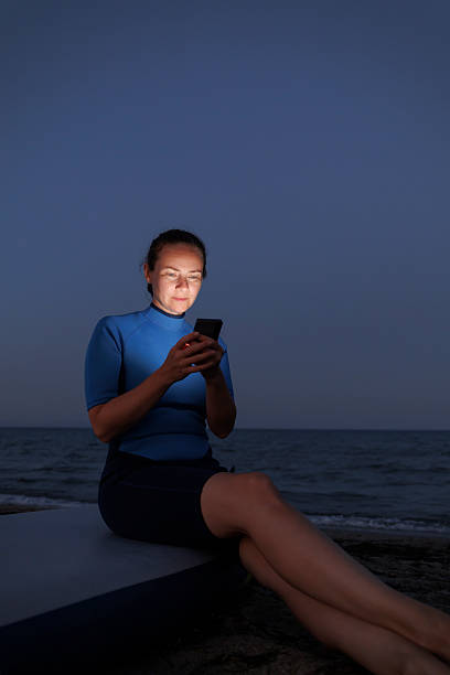 istock Woman sitting on SUP board and using smart phone at beach at dusk 2227206647