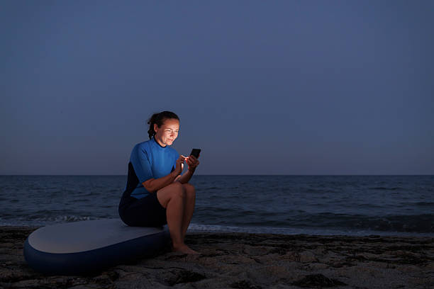 istock Woman sitting on SUP board and using smart phone at beach at dusk 2227206687
