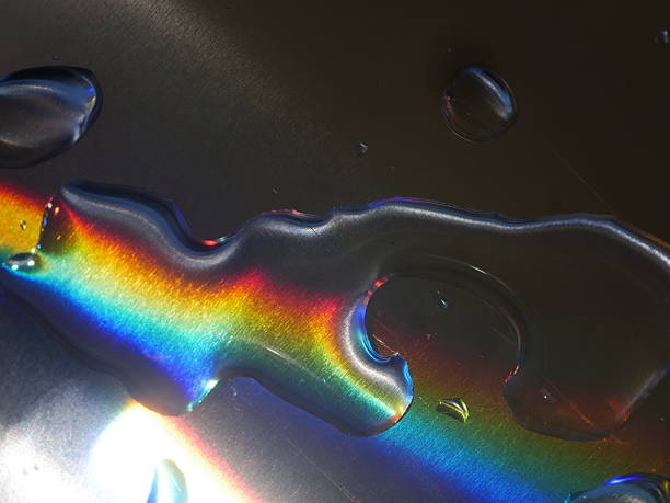 Rainbow is reflected in a puddle of water. The water droplets are scattered across the surface, creating a shimmering effect. The rainbow appears to be a symbol of hope and positivity