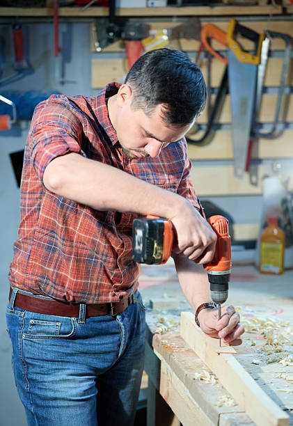 Carpentry and woodworking as a hobby and craft. Attractive young man dressed in red plaid shirt and in jeans. The man is working with work carpenter tools.  Shooting in a home workshop