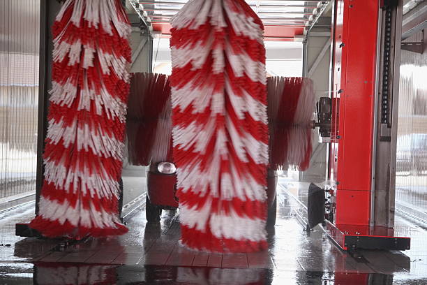 Car is being cleaned with a red and white brush in a car wash. The brush is moving back and forth, covering the car with water and soap