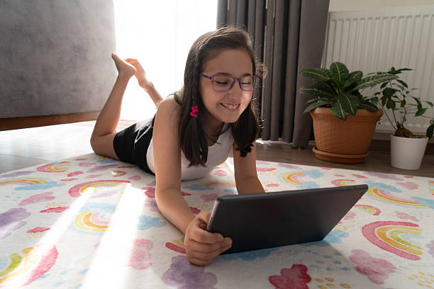 istock Little girl using a digital tablet while lying on the floor at home 2227210624