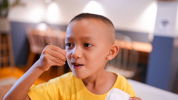 istock Young boy enjoys delicious meal, smiling as he takes bite with fork. cozy restaurant setting adds to joyful atmosphere, making it delightful dining experience 2227211191