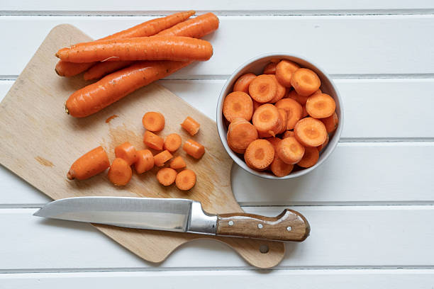 Fresh carrots with sliced ones on wooden background