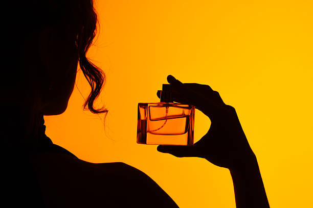 istock Woman Silhouette Holding Perfume Bottle on Orange Background 2227212084