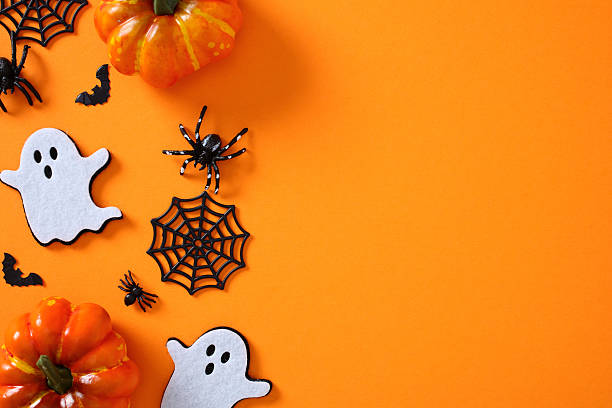 istock Halloween flat lay on vivid orange background featuring pumpkins, ghost cutouts, bats, spiders, and webs clustered on the left side 2227218145