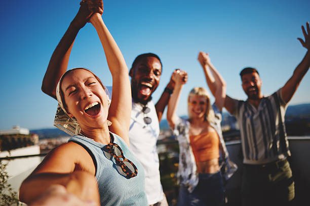 Cheerful multi-ethnic friends holding hands and celebrating on a rooftop party