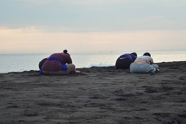 Maintaining their pose in quiet concentration, the girls continue holding their full forward stretch on the sand, reflecting peace and focused breath.
