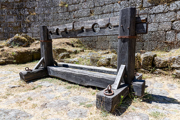 A wooden structure with a metal chain hanging from it. The chain is attached to a wooden post. The structure is old and worn, and it is a form of punishment. Scene is somber and foreboding