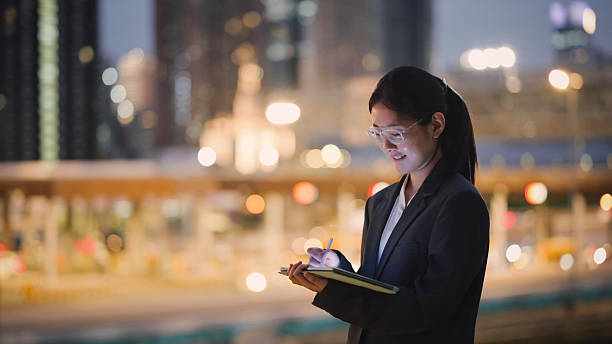 istock Asian young woman using smartphone against city skyline backdrop  future connection and human-ai interaction  in mobile experience with night cityscape, blending urban lifestyle and ai-powered apps 2227229779