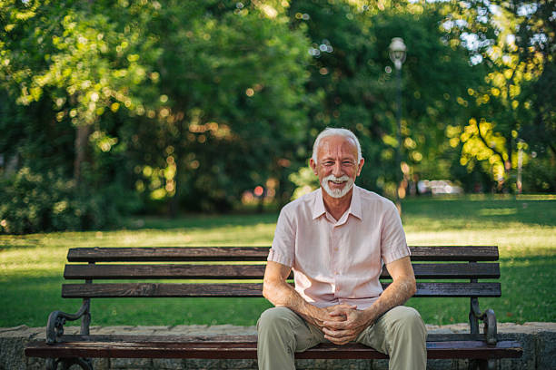 istock Senior man smiling while relaxing on park bench 2227231996
