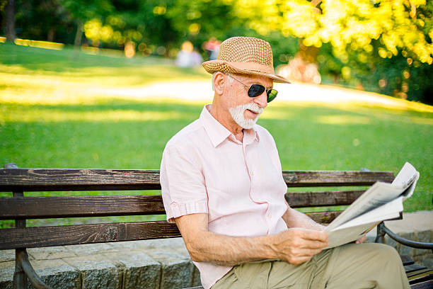 Elderly man enjoying reading newspaper in park on sunny summer day