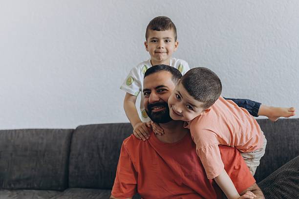 istock Happy middle eastern father having fun with his three sons at home. Dad cuddling toddler while other kids play and smile. Loving family moment on cozy sofa 2227232895