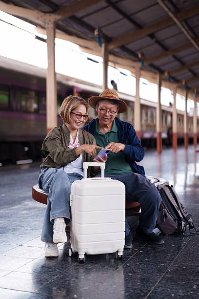 istock Active older Asian couple smiling using smartphone platform train station planning exciting leisure travel journey holiday trip vacation adventure digital technology 2227233987