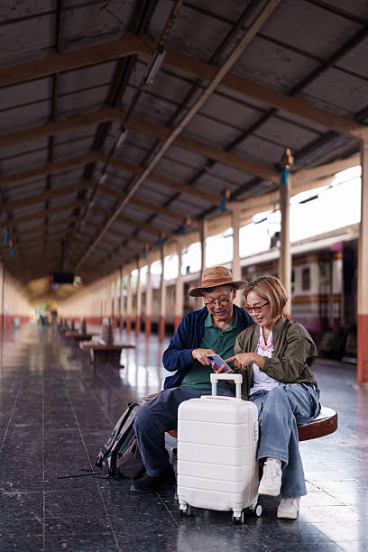 istock Older Asian Couple Using Smartphone Planning Travel Train Station Platform 2227233992