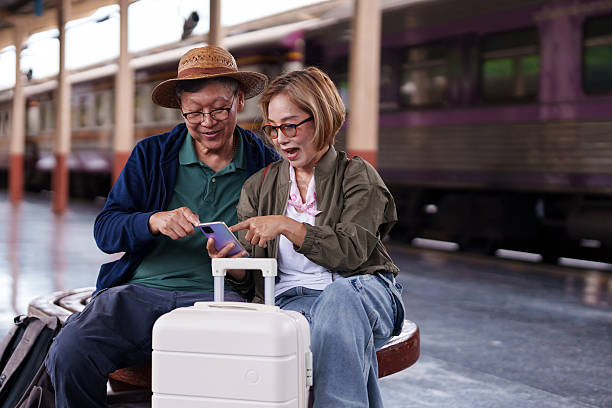 istock Older Asian couple enjoy train station travel planning using smartphone technology 2227234005