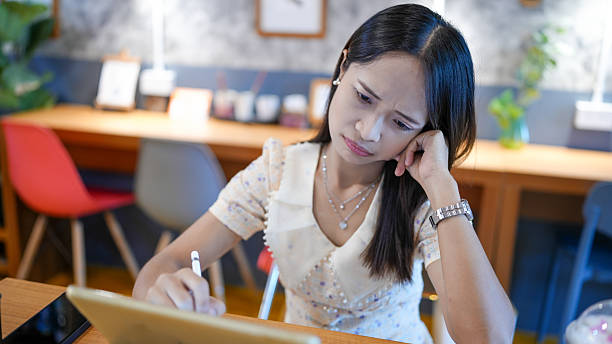 Young woman is thoughtfully writing on tablet in cozy cafe setting, showcasing concentration and creativity. warm ambiance enhances her focused expression