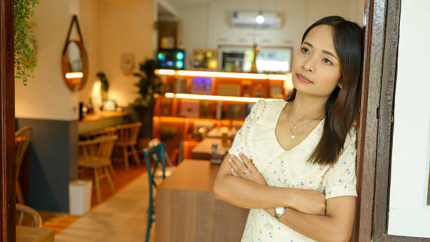 Thoughtful woman stands in cozy cafe, gazing out with contemplative expression. warm interior features wooden furniture and soft lighting, creating welcoming atmosphere