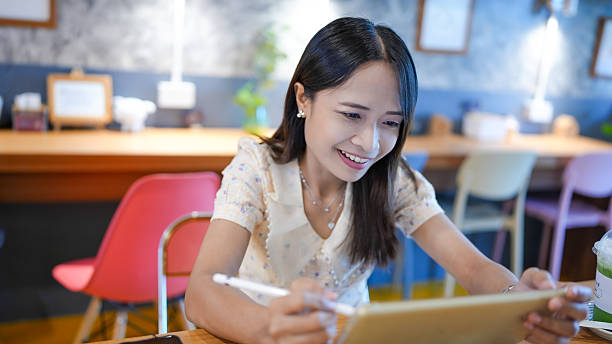 istock Young woman smiling while using tablet in cozy cafe, showcasing relaxed atmosphere and modern interior design. scene captures joy and creativity 2227238494