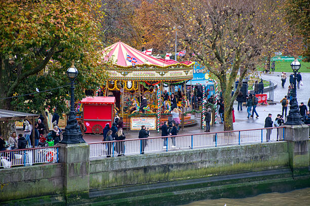People brighten a rainy fall day along with a colorful carousel on the Queens Walk, near the London Eye.  The Golden Carousel is a replica of a traditional English Carousel that was at the 1951 Festival of Britain, in Battersea Park.