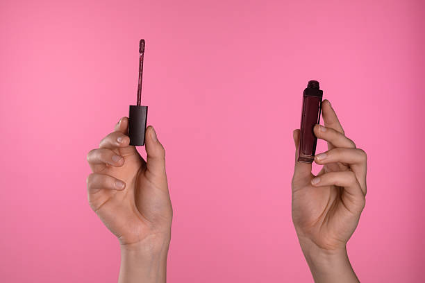 istock Two Hands Holding Lip Gloss On Pink Background 2227239079