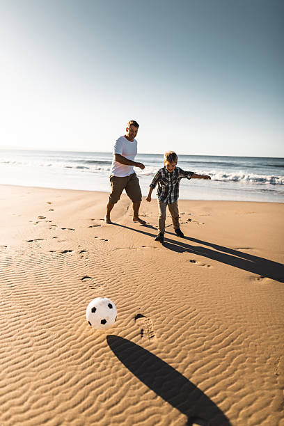 istock dad and son playing soccer on the beach 2227245311