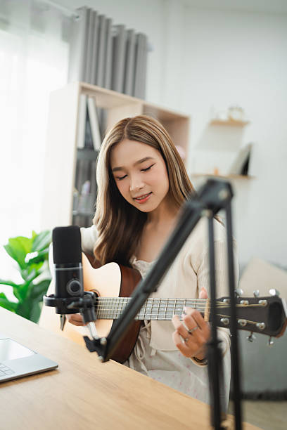 istock Young woman playing guitar and singing in a modern home studio, microphone and laptop on table, creative atmosphere, focus on music and passion 2227247827