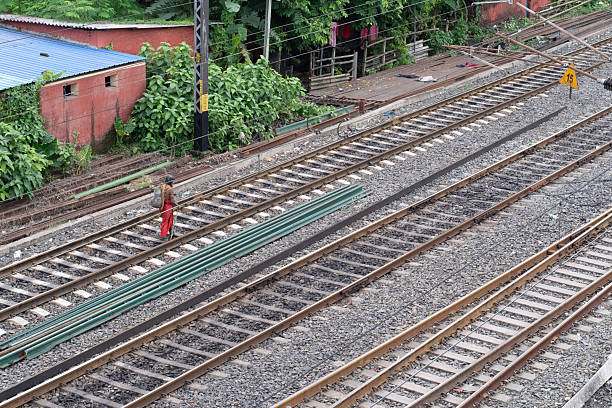 sonarpur, west bengal, india- july 27, 2025: \nan Indian holy man, dressed in a traditional red cloth walks barefoot along railway tracks with green metal rods lying beside, captured from above, the image juxtaposes spiritual simplicity with urban infrastructure, highlighting contrasts in modern Indian life.
