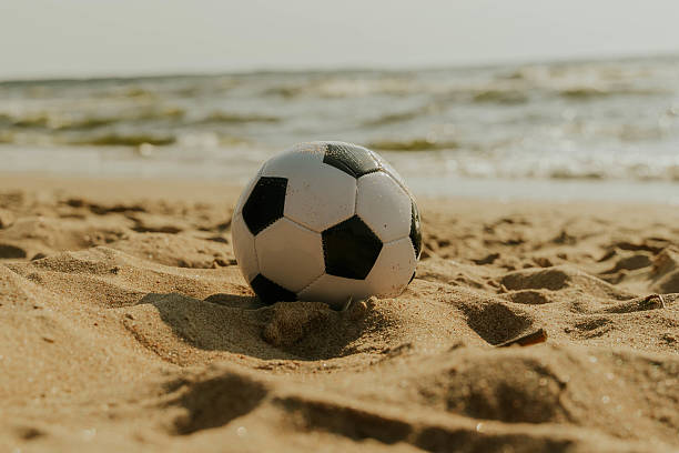 istock Soccer ball resting on sandy beach by ocean waves 2227250142