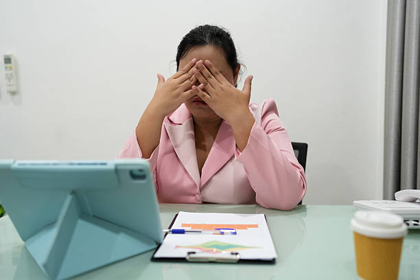 istock Asian businesswoman feeling exhausted while working late in office, hand on forehead, showing workplace fatigue and emotional burnout from stressful workload. 2227257686