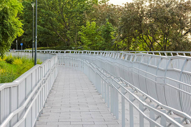 istock Long pedestrian bridge pathway with metal mesh fencing creating linear perspective toward green landscape 2227260471