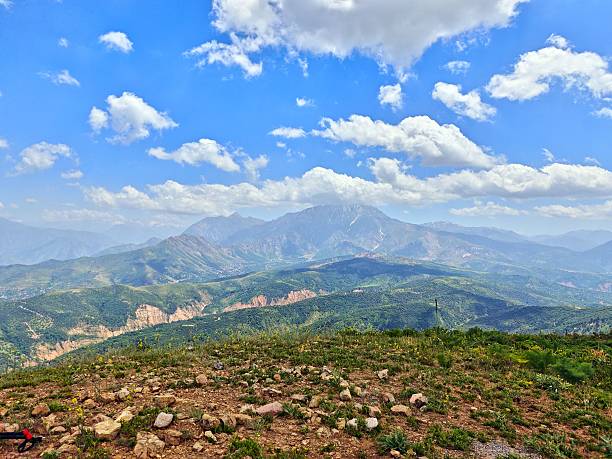 A breathtaking mountain landscape under a vibrant blue sky with fluffy clouds, showcasing lush green valleys and rocky terrain.