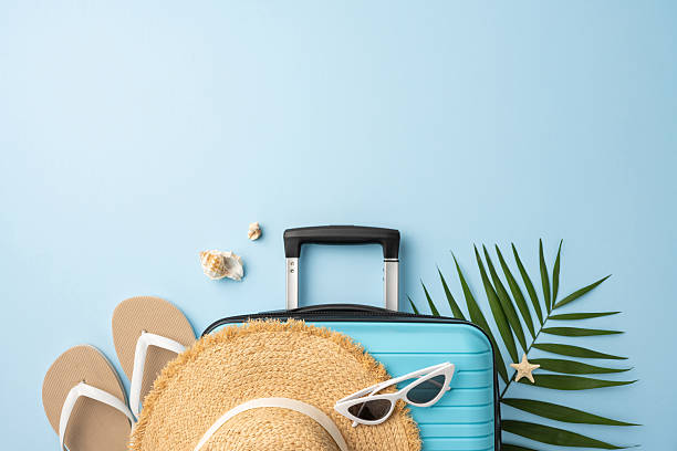 istock Travel-themed image showing a suitcase, sandals, hat, sunglasses, and tropical elements on a blue background 2227284178