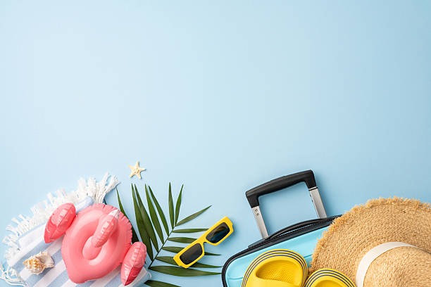 istock Flat lay composition featuring summer travel items including a suitcase, sun hat, flip-flops, and tropical decorations on a blue background, evoking vacation vibes and the warm season 2227284180