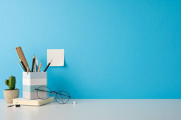 istock Stylish desk arrangement featuring glasses, pencils, and notepad against a solid blue backdrop 2227284205