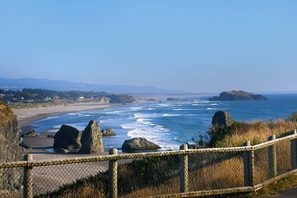 Safety fence prevents visitors, to Bandon Beach, Oregon, from getting too close to edge of cliff.  But view from overlook is stunning with blue water and sea stacks.