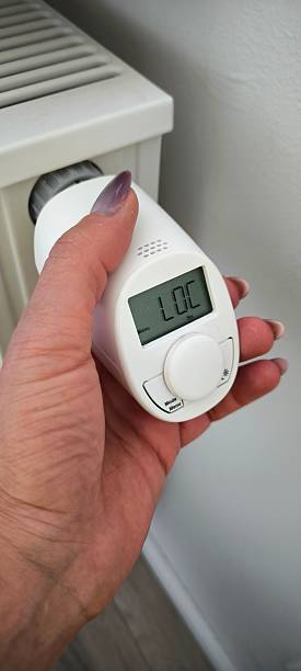 istock Smart thermostat: a woman's hand adjusts a modern thermostat on a heating radiator 2227288404
