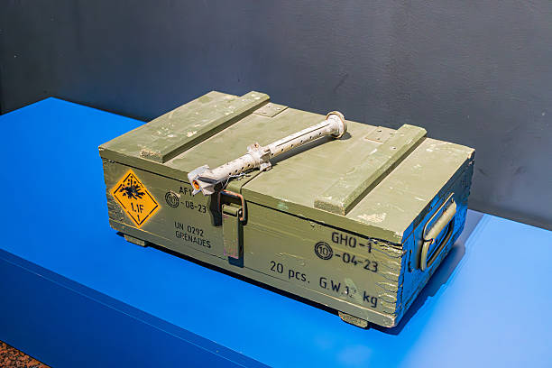 Green metal military storage box with ammunition, placed on a blue platform, indoors under even lighting, yellow hazard labels. a