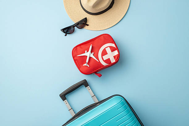 istock Vacation items including a hat, sunglasses, a first aid kit, and a suitcase on blue 2227288855