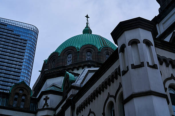 Two eras are engaged in a quiet dialogue in a corner of Ochanomizu, Tokyo. The graceful curves of the historic St. Nicholas Cathedral (Tokyo Resurrection Cathedral) and the sharp glass walls of the adjacent Ochanomizu Sola City. The stately atmosphere of the stone and concrete and the light expression of the glass reflecting the sky create a vivid contrast under the cloudy sky. It is a scene unique to the city, where more than a century of changes in architectural thought are engraved in a single frame.