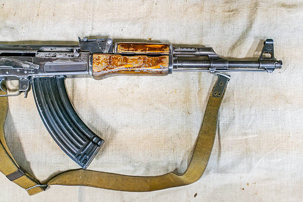 AK-47 assault rifle, horizontally placed on light beige fabric, wooden handle contrasting with dark matte metal barrel, signs of use, natural lighting casting soft shadows